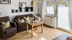 Een gezellige woonkamer met een bruine zithoek, een houten salontafel en een boekenkast met boeken en decoratieve spullen.
