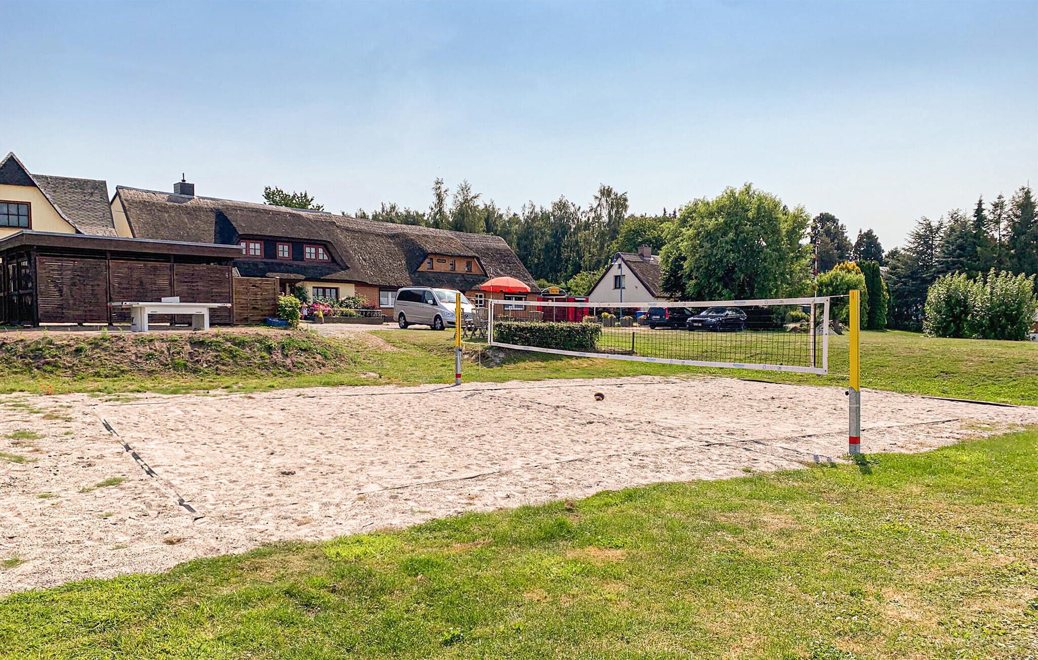Un terrain de volley-ball sablonneux, avec un filet, entouré d’une zone herbeuse et d’un bâtiment à toit de chaume.