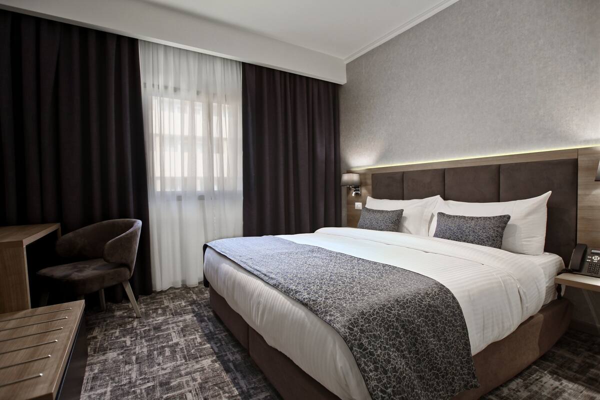 A hotel room with a large bed, a desk, a chair, and a window with curtains.