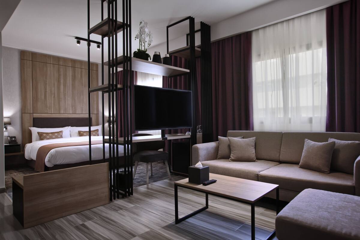 A modern hotel room with a bed, sofa, TV, and a desk.