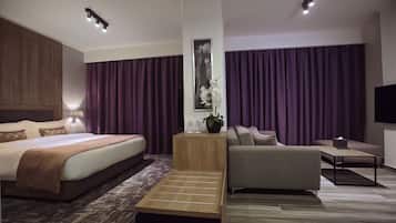A modern hotel room with a large bed, a sofa, a coffee table, and a TV.