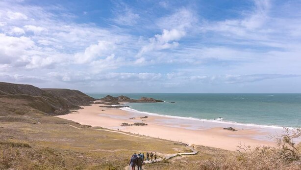 Eine Küstenlandschaft mit Sandstrand, Felsformationen und blauem Himmel.