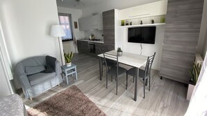 Ein modernes, kompaktes Wohnzimmer mit Essbereich, Küchenzeile und einem an der Wand befestigten Fernseher.