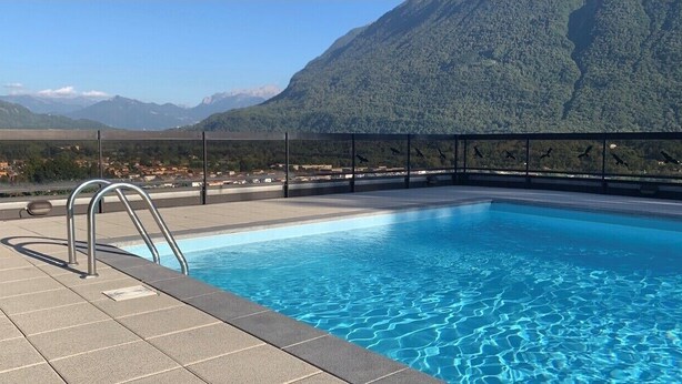 Ein Schwimmbecken mit Metallleiter, umgeben von einer gefliesten Terrasse, mit Blick auf eine Berglandschaft im Hintergrund.