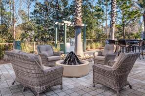 Relax in a cozy outdoor space with a fire pit, wicker furniture, and a pergola.