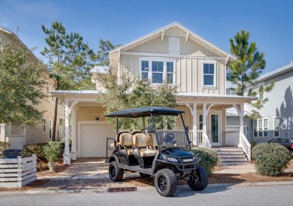 A two-story house with a covered garage, a driveway, and a golf cart parked in front. - Beargrass -Luxury NatureWalk Home - Golf Cart (Santa Rosa Beach)