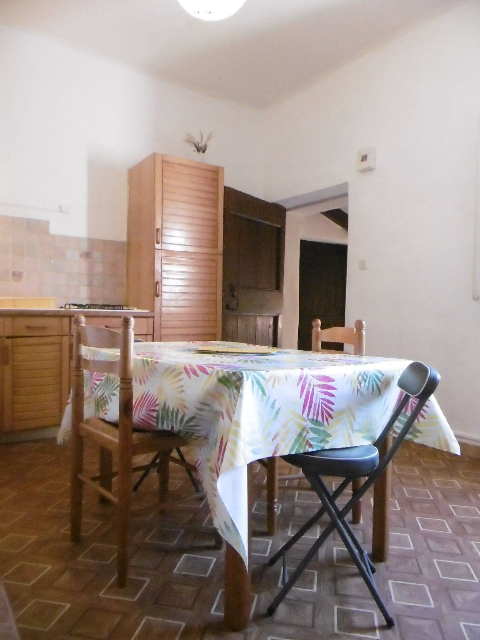 A dining area with a table covered by a tropical leaf tablecloth, wooden chairs, and a wooden cabinet.