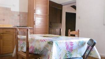 A dining area with a table covered by a tropical leaf tablecloth, wooden chairs, and a wooden cabinet.