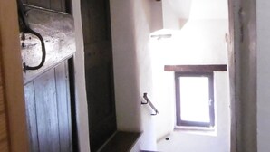 Un pasillo estrecho con una puerta de madera a la izquierda, un ventanal pequeño al final y una escalera que sube a un nivel superior.