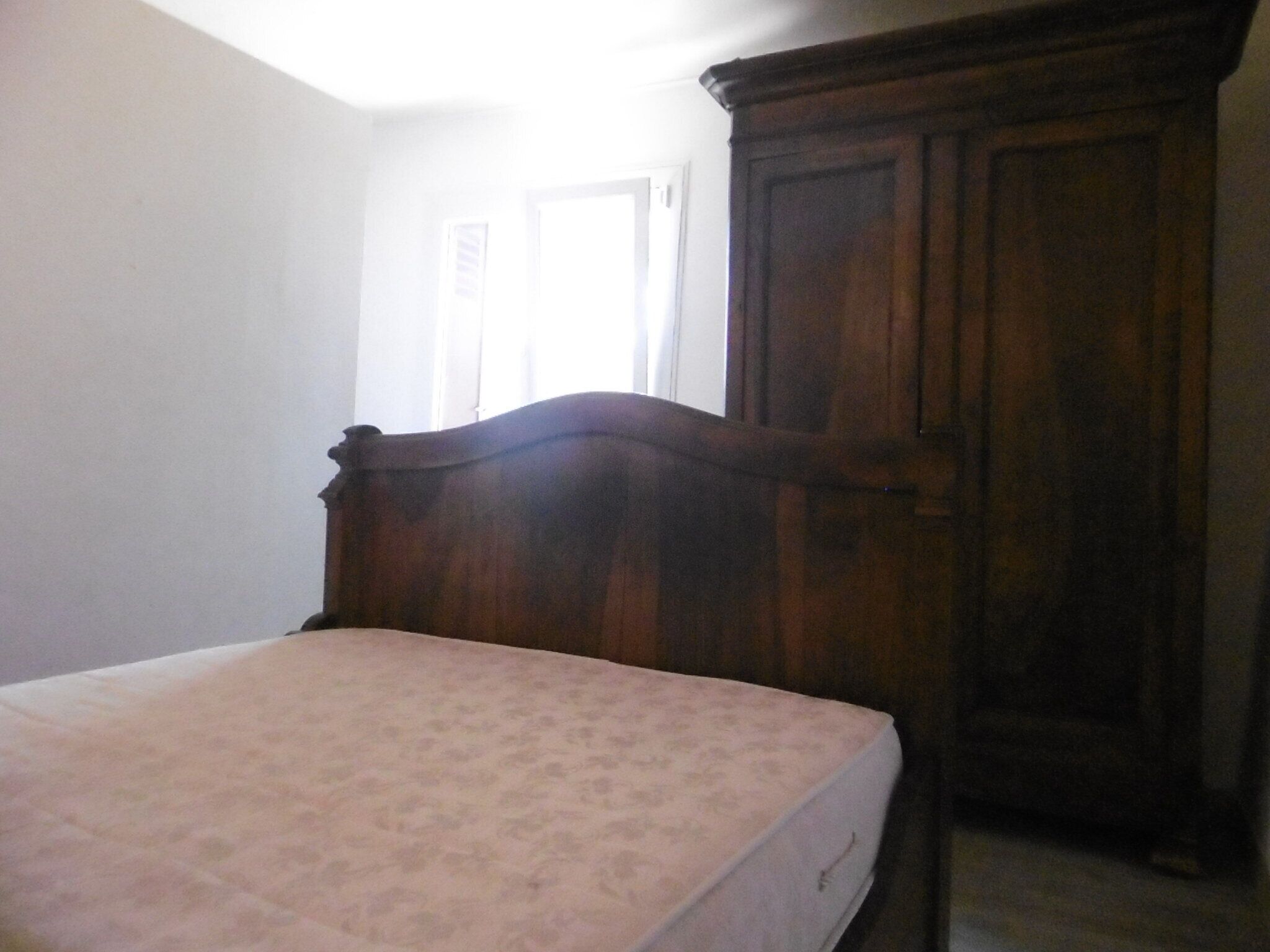 Ein Schlafzimmer mit einem hölzernen Bettgestell, einem Kleiderschrank und einem Fenster mit Vorhängen.