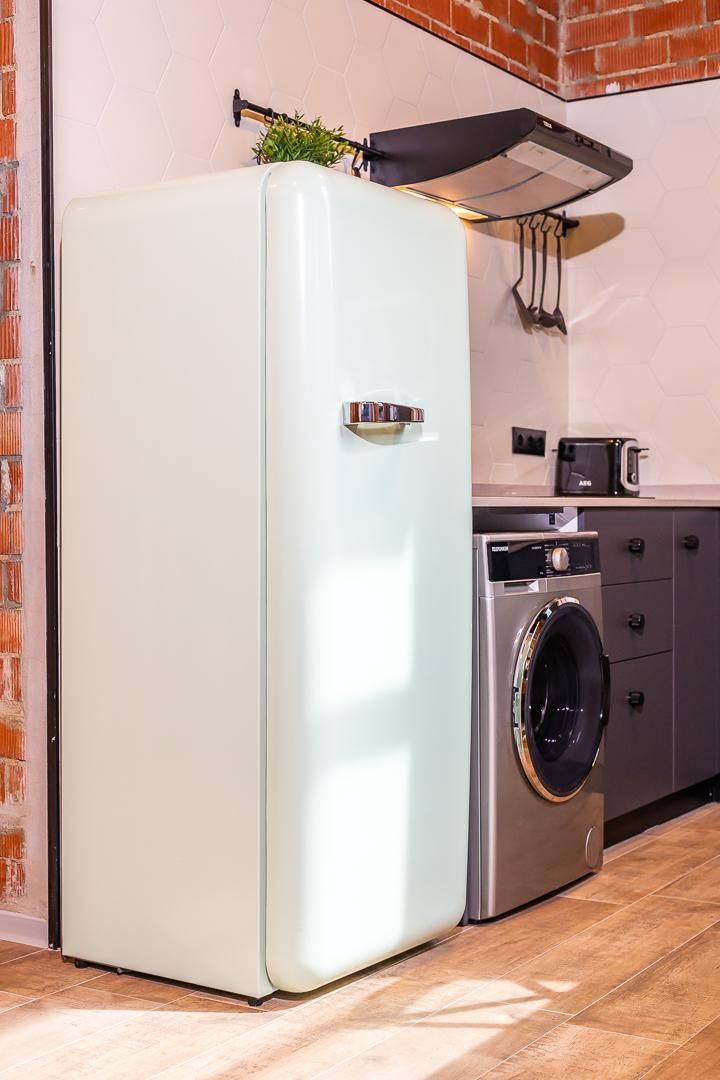 Eine kompakte Küche mit einem weißen Kühlschrank, einer integrierten Waschmaschine und einer Mikrowelle auf der Arbeitsfläche.