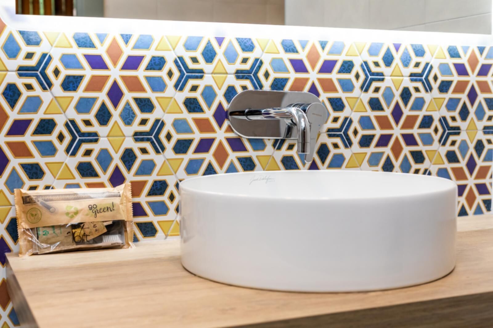 Un baño con lavamanos blanco, un grifo moderno y un salpicadero de azulejos geométricos y coloridos.