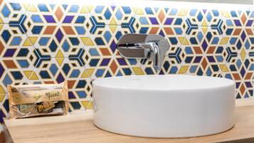 Un baño con lavamanos blanco, un grifo moderno y un salpicadero de azulejos geométricos y coloridos.