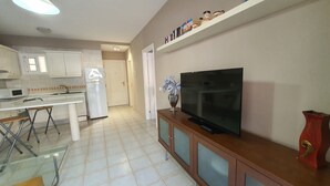 A modern kitchen with white cabinets, a white refrigerator, and a TV on a wooden cabinet.