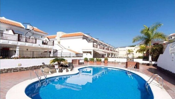 A swimming pool surrounded by buildings with balconies and a clear blue sky.