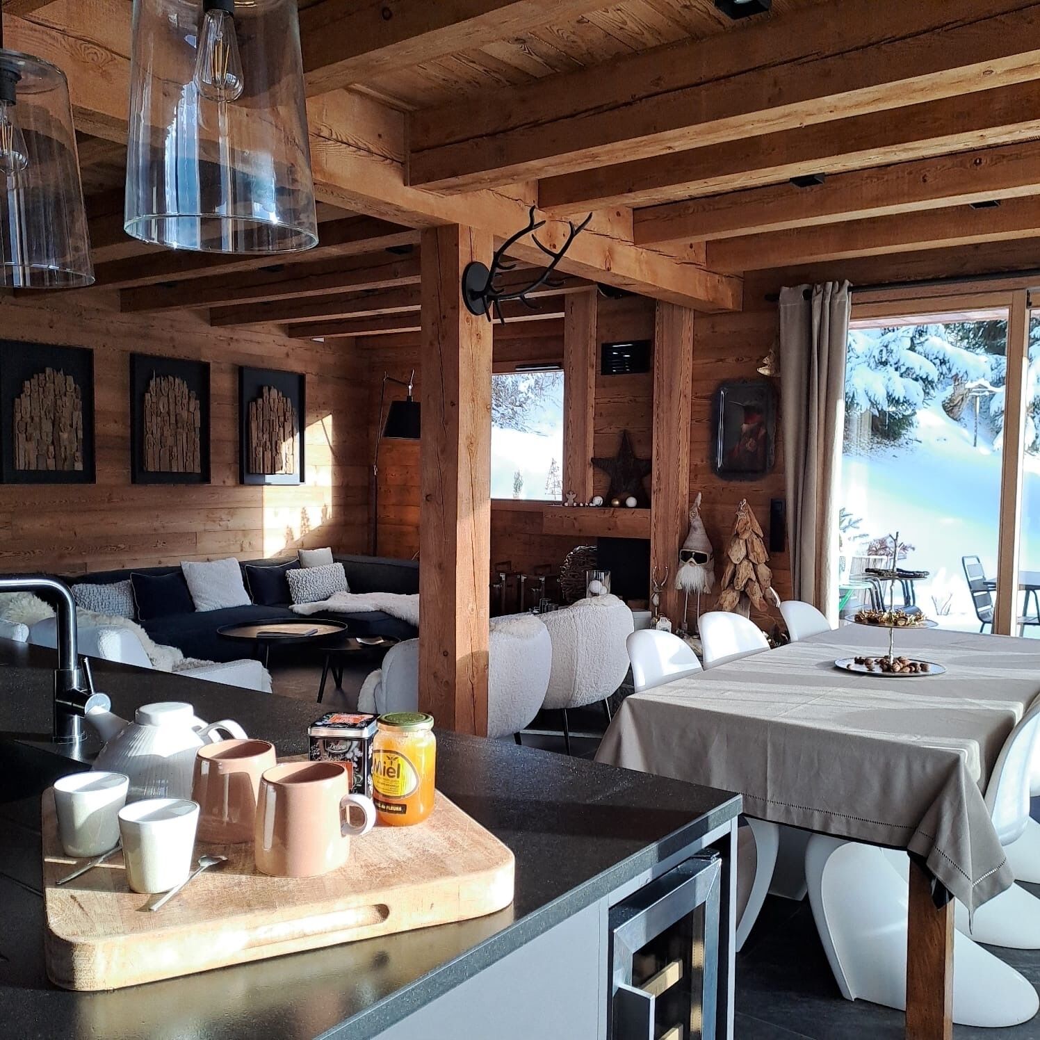 L’intérieur chaleureux d’un chalet, avec un revêtement mural en bois, un coin repas comprenant une table et des chaises, et un espace cuisine équipé d’une planche à découper et d’ustensiles.