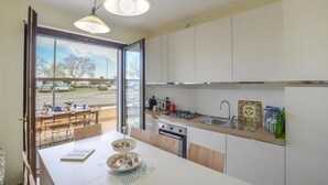 A modern kitchen with a large island, a gas stove, and a sink. There is a dining area with a table and chairs visible through a glass door.