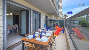 An outdoor dining area with a table set for four, a children's play area with slides, and a view of the street and parked cars.
