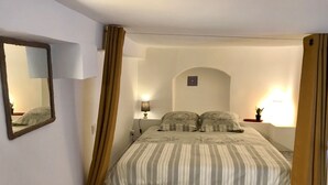 Ein Schlafzimmer mit einem Bett, einem Nachttisch, einer Lampe, einem Spiegel und einem Fenster mit Vorhängen.