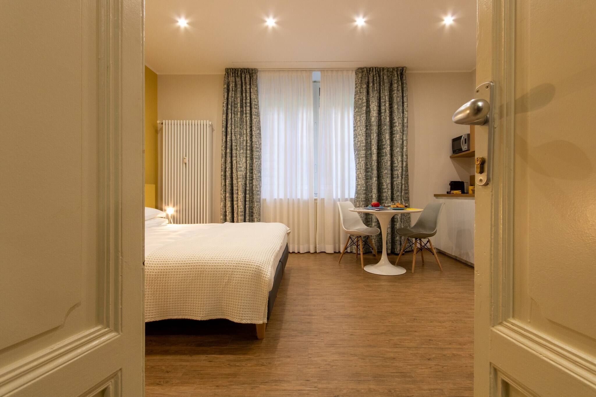 Habitación de hotel con cama, una mesita con sillas, un radiador y cortinas.