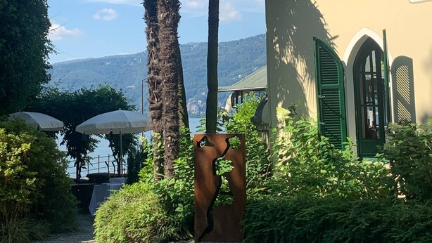 A building with green shutters, a palm tree, and a view of the mountains. - Beautiful Apartment in Piemonte - Wifi Free (Verbania)