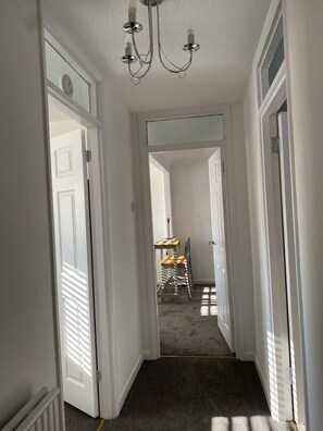 Um corredor com paredes brancas, um candelabro e uma área de jantar com mesa e cadeiras.