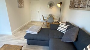 Una sala moderna con un sofá seccional gris oscuro, una mesa de centro de madera y un comedor con mesa y sillas de vidrio.