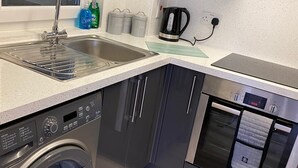 Cocina compacta con un lavamanos de acero inoxidable, lavadora integrada, cafetera y microondas.