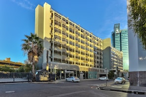Un hotel de varios pisos con una fachada moderna, una entrada visible y un estacionamiento con coches.