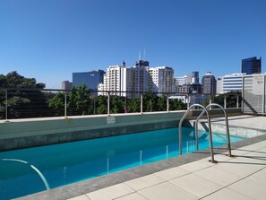 Una piscina en la azotea con vistas a la ciudad, una escalera de metal y un cartel advirtiendo contra la retirada del limpiafondos.