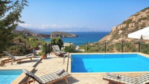 Une piscine avec des chaises longues, une vue sur la mer et un paysage montagneux.