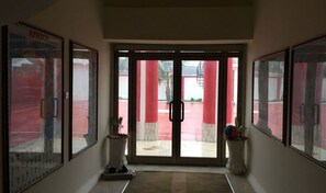 A hallway with framed pictures on the walls, a door leading outside, and a small plant in a vase. - Rasta Tees Place - Standard (Adenta)