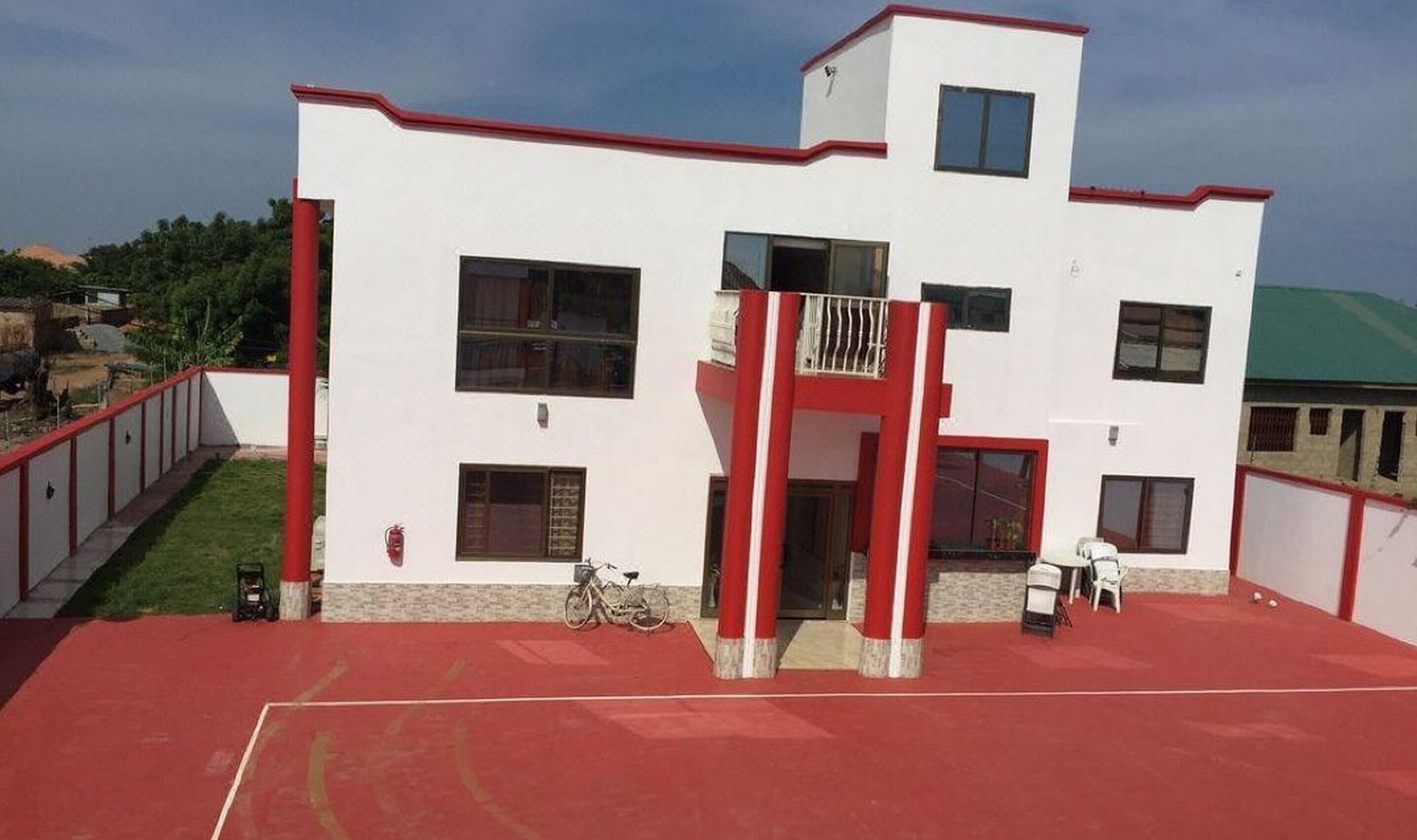 A two-story building with a red and white exterior, a balcony, and a red sports court in front.