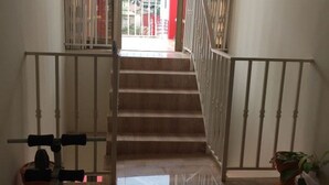 A staircase with white balusters and a handrail, leading to a bright area with a red door. - Rasta Tees Place, Presidential Apartment (Adenta)