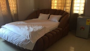 A bed with a headboard, a bedside table, and a window with curtains. - Rasta Tees Place, Presidential Apartment (Adenta)