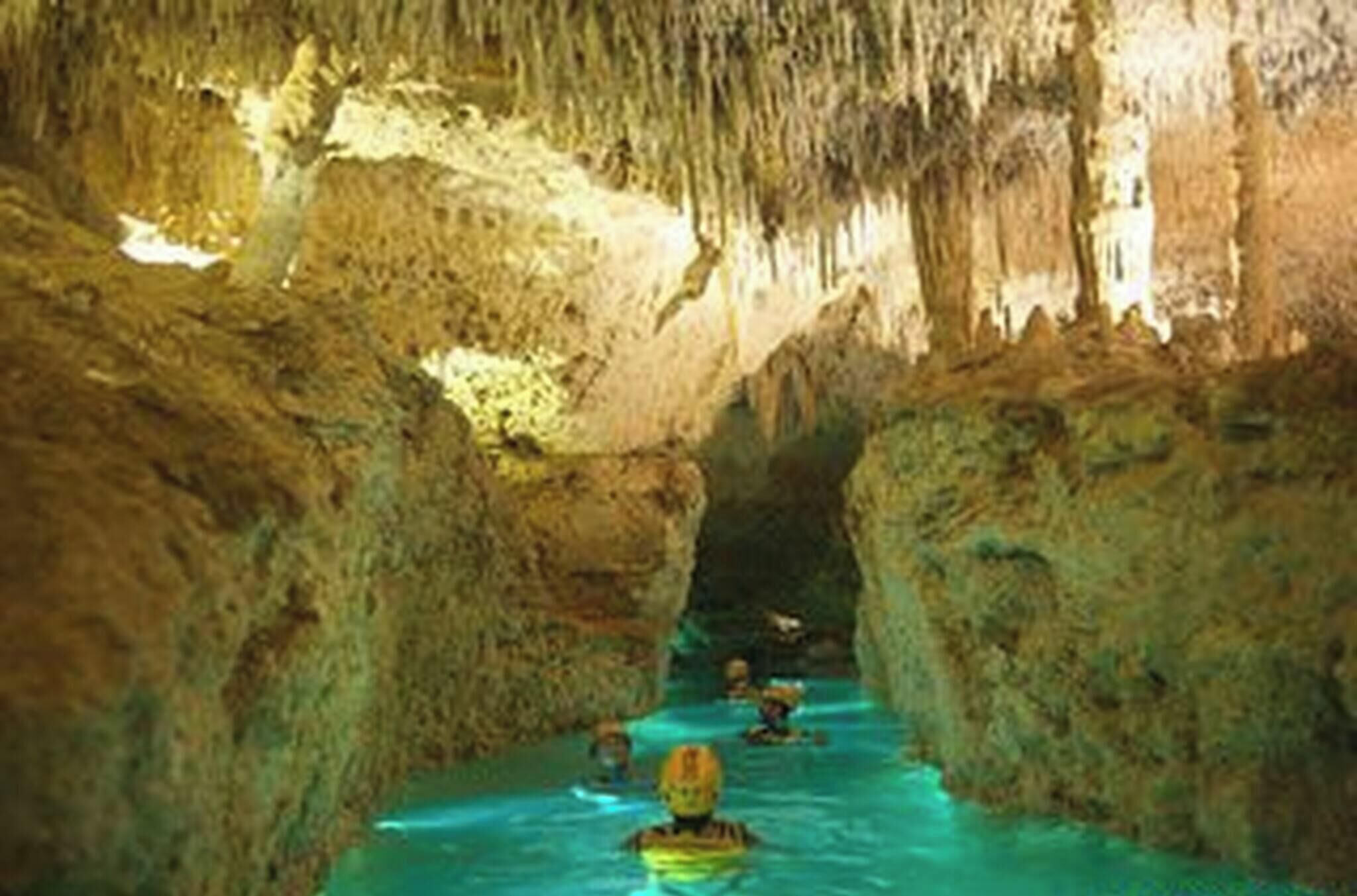 Cueva con estalactitas y estalagmitas, agua corriendo por un estrecho pasadizo y gente nadando.