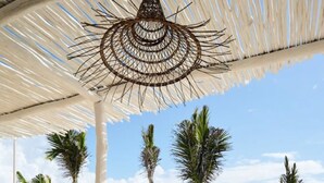 Un área de estar al aire libre con una mesa, sillas, un toldo de paja y palmeras.