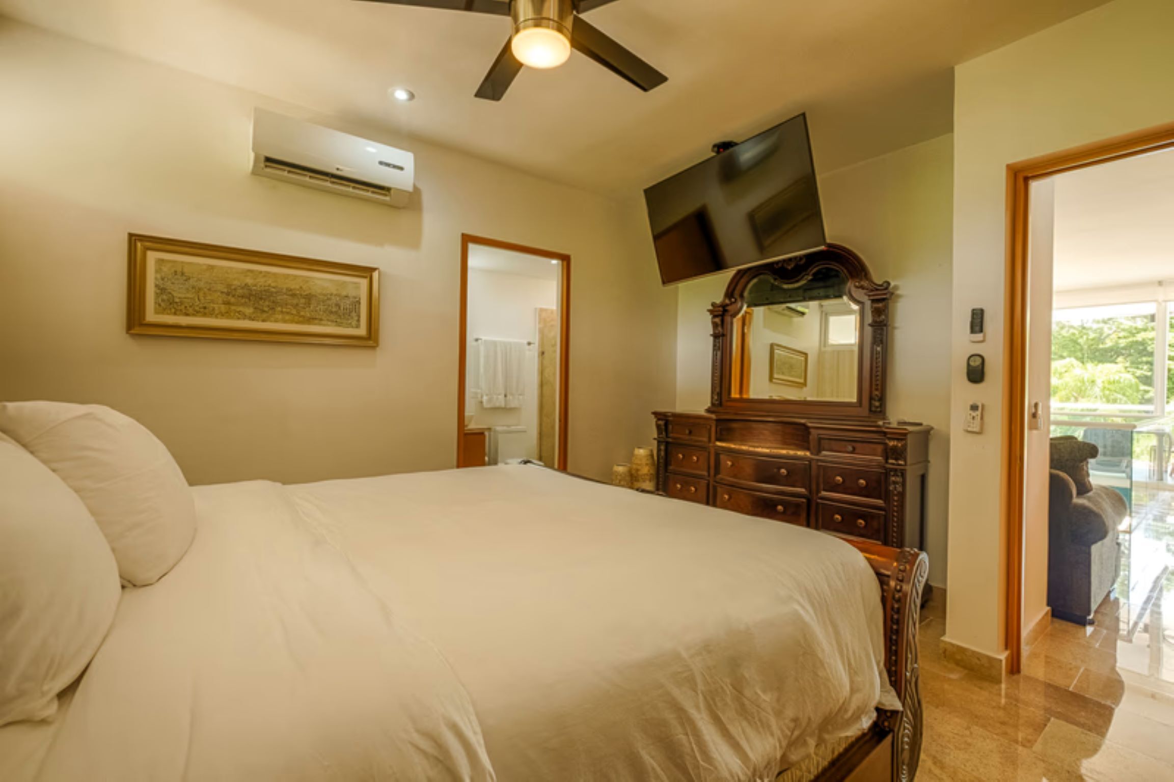 A bedroom with a bed, a ceiling fan, a dresser, a TV, and a door leading to a balcony.