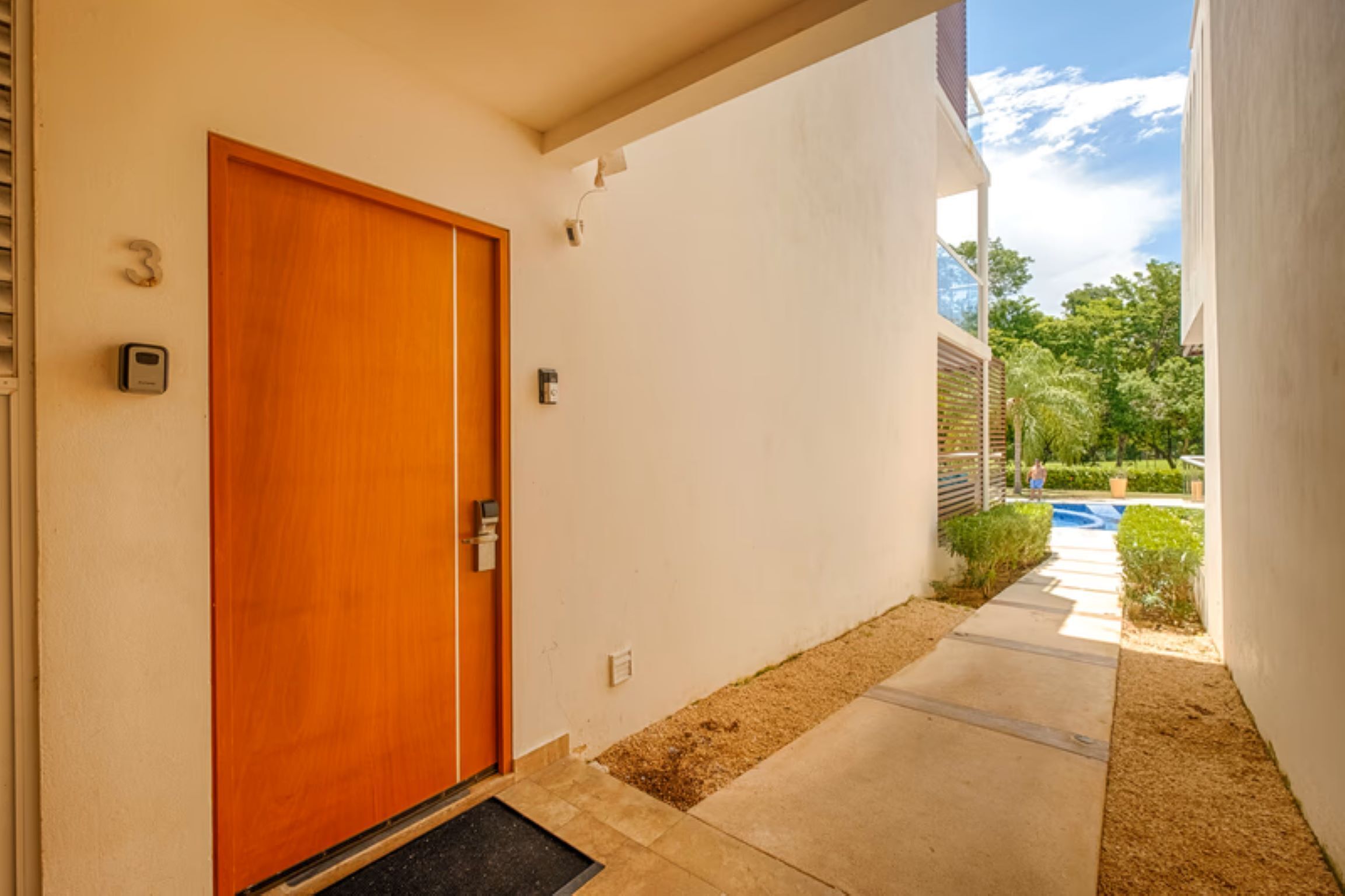 A modern building with a wooden door, a small outdoor area with a pathway, and a clear sky.