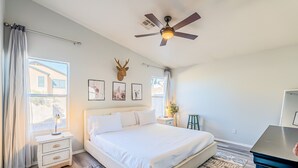 A bedroom with a bed, bedside tables, a ceiling fan, and a window with curtains. - Three bed two bath, gas grill, king bed (Tucson)