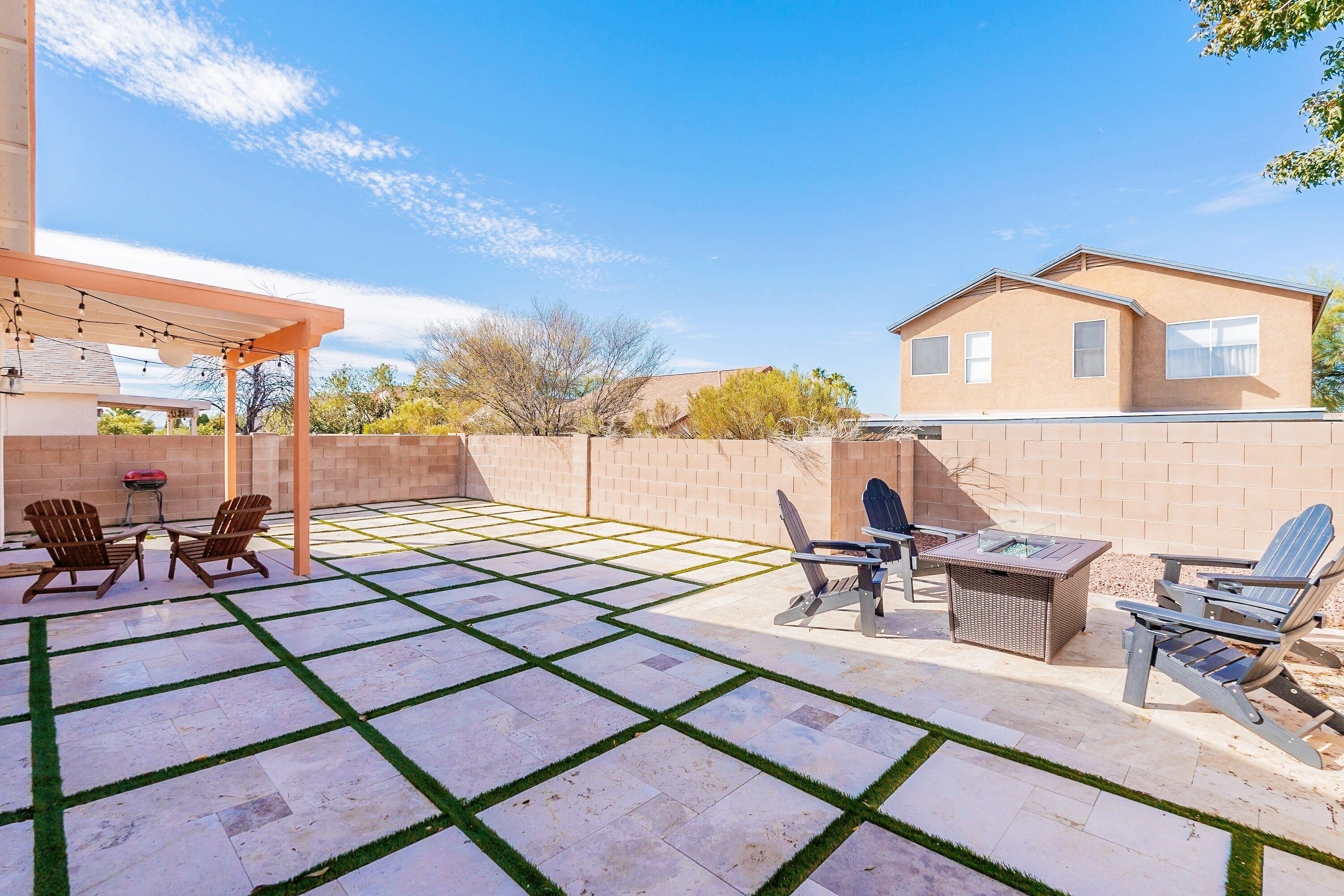 Eine Terrasse mit einer Pergola, Sitzgelegenheiten im Freien und einem Grill.