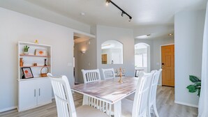 A dining area with a wooden table and white chairs, a white cabinet with decorative items, and a door leading to another room. - Three bed two bath, gas grill, king bed (Tucson)