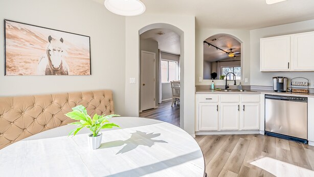 A modern kitchen with white cabinetry, a dining area with a round table and a tufted bench, and a hallway leading to a dining room. - Three bed two bath, gas grill, king bed (Tucson)