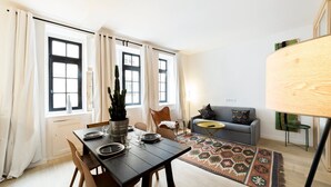 Una sala de estar moderna con comedor, que incluye una mesa de madera para cuatro personas, un sofá gris y una alfombra estampada.