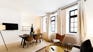 Una sala de estar moderna con comedor, ventanas amplias, un televisor de pantalla plana y una zona de estar acogedora.