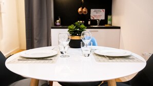 Una mesa redonda de comedor con dos platos blancos, dos copas de vino y una pequeña planta en maceta.