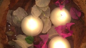 Una ciotola di legno con candele e petali di fiori.