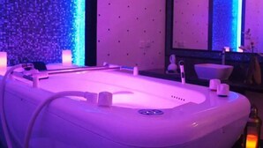 Una stanza spa con una vasca da bagno bianca e grande, un lettino da massaggio fissato al muro e un piccolo lavandino.