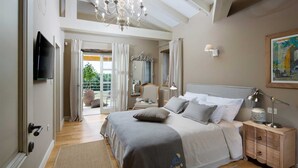 A bedroom with a large bed, a nightstand, a TV, and a chandelier.