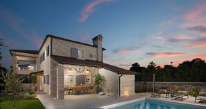 A two-story stone house with a swimming pool, outdoor seating, and a garden.